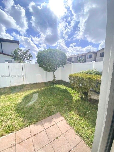 Enclosed backyard featuring a concrete paver patio, manicured lawn, established landscaping, and white vinyl perimeter fencing