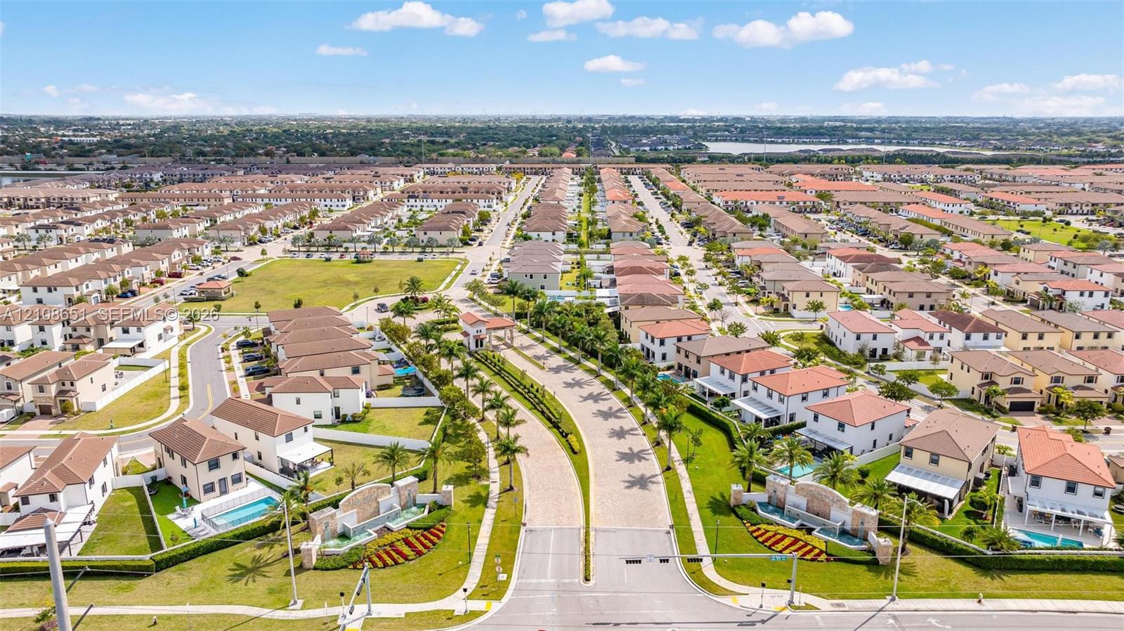 Aerial perspective of a residential community featuring paver-surfaced roadways, landscaped entry monuments with water features, tree-lined thoroughfares, and private swimming pools