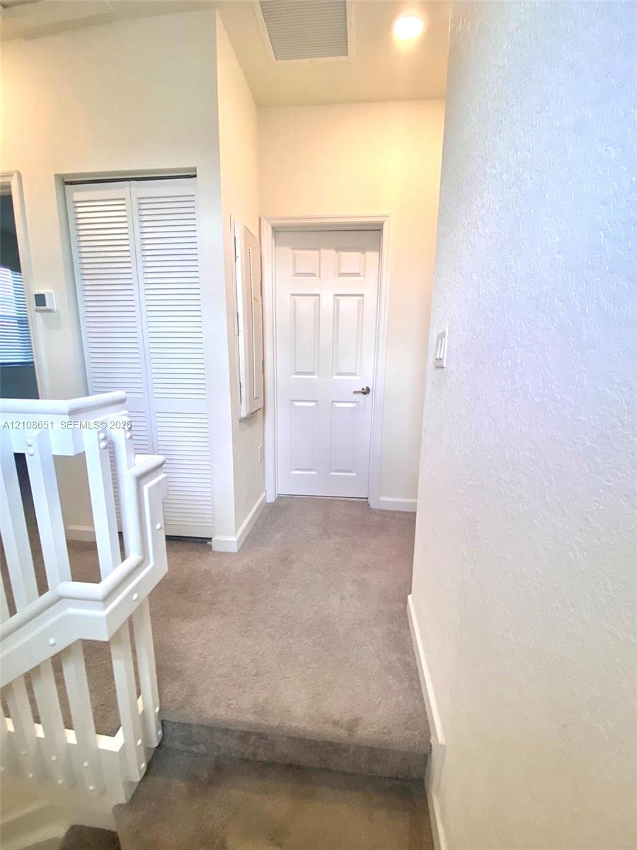 Neutral-toned carpeted flooring, white six-panel interior door, and bi-fold louvered closet doors featuring a white finish