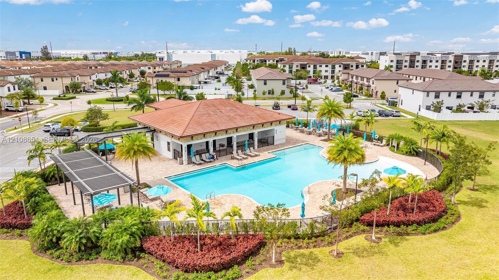 Community amenity area featuring a swimming pool, covered pavilion with shingle roof, expansive paver deck, and manicured landscaping