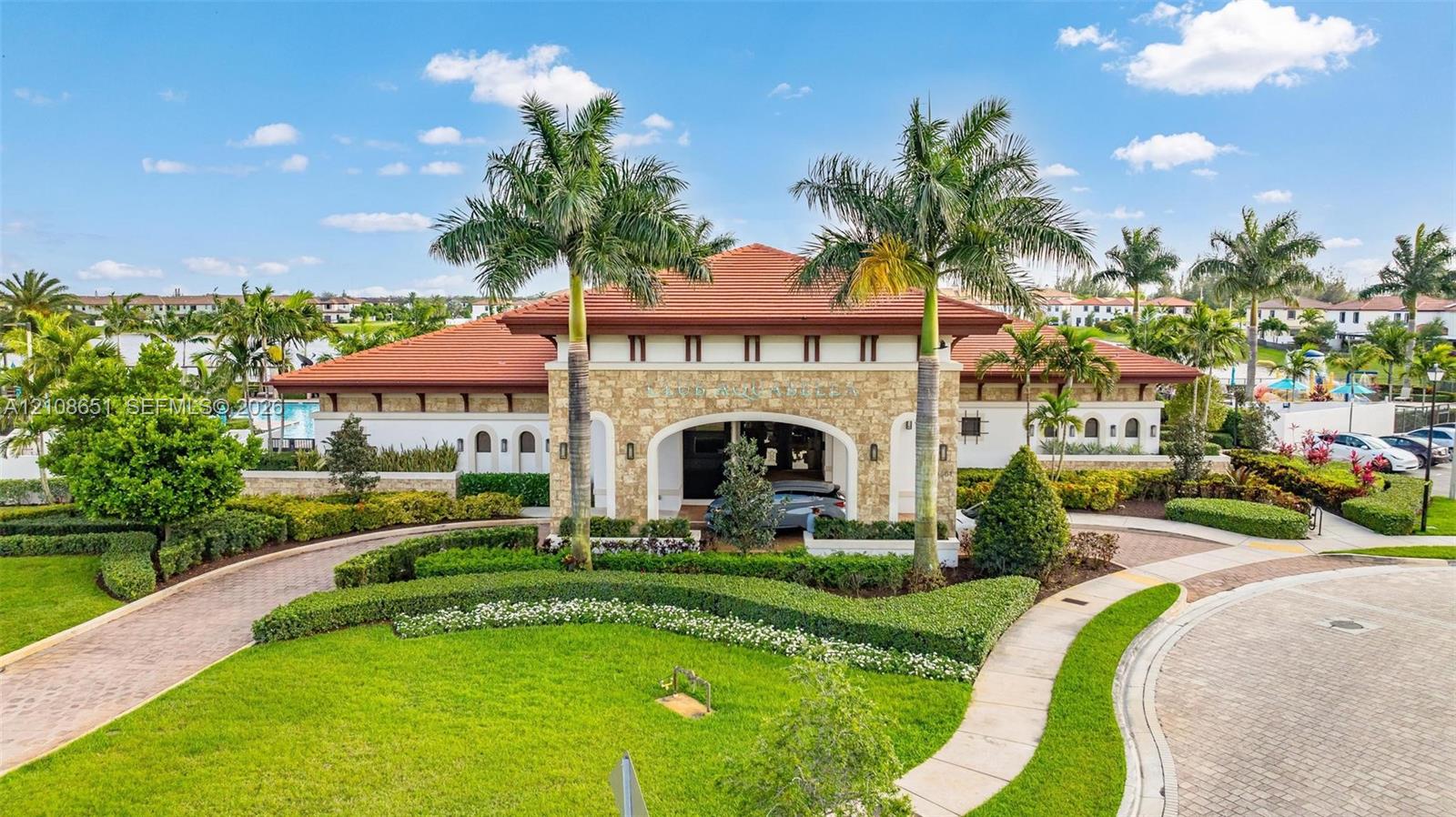 Mediterranean-style exterior featuring stone veneer siding, a tile roof, a covered porte-cochre, and professionally manicured landscaping