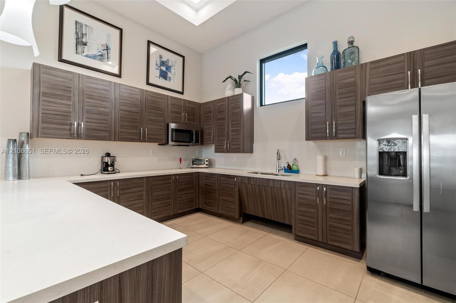 Kitchen featuring horizontal-grain wood cabinetry, white stone countertops, stainless steel appliances, tile flooring, and high ceilings with recessed lighting