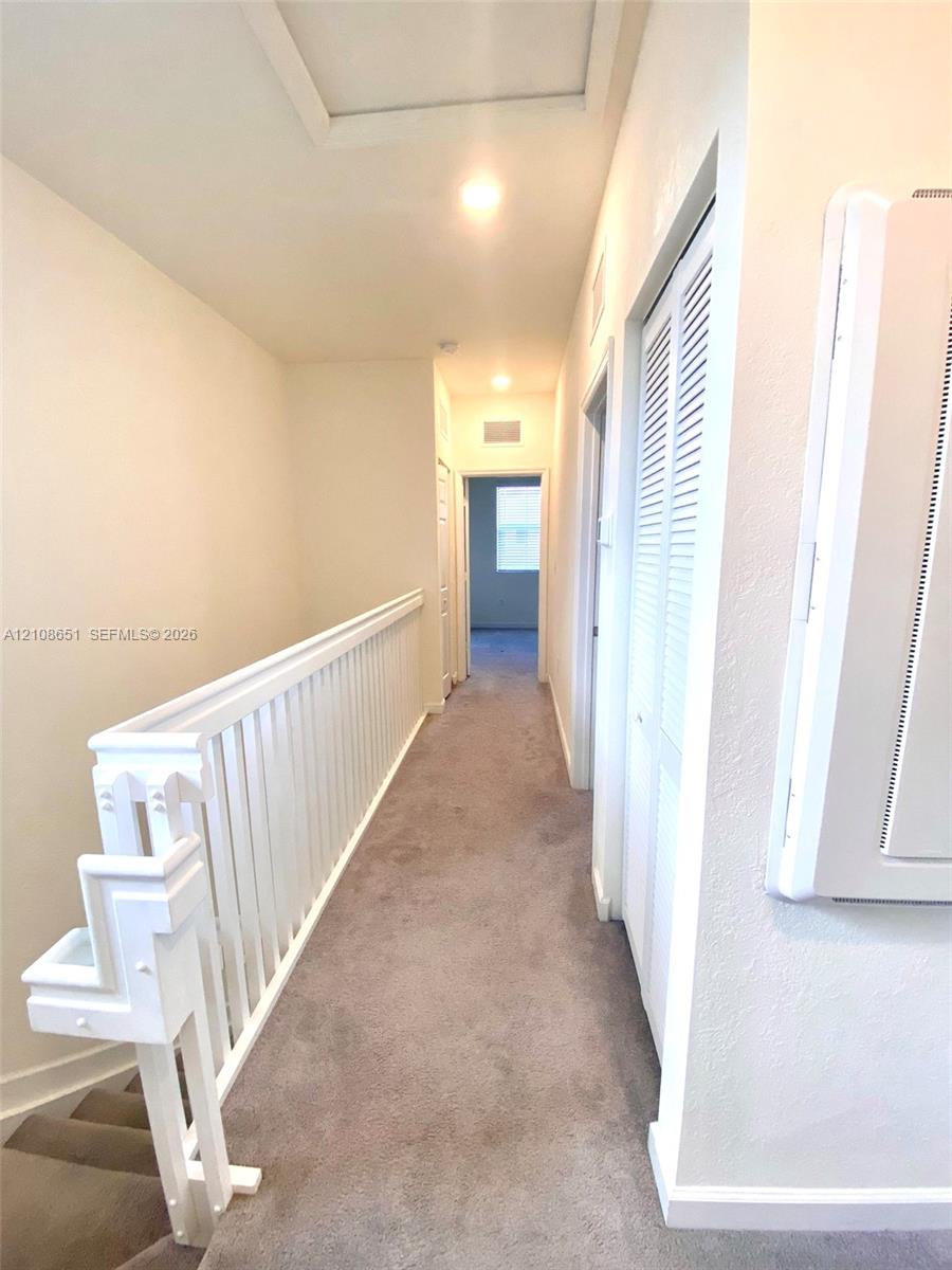 Hallway featuring neutral carpeting, a white-painted wooden balustrade, and louvered bifold closet doors