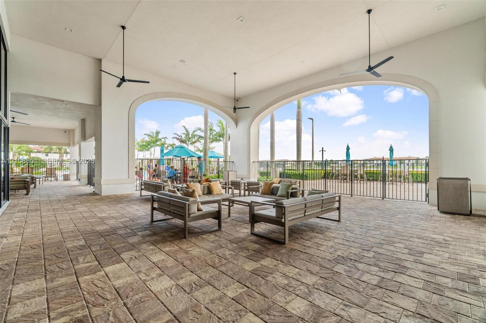 Covered patio featuring stone-paver flooring, multiple ceiling fans, and arched architectural openings
