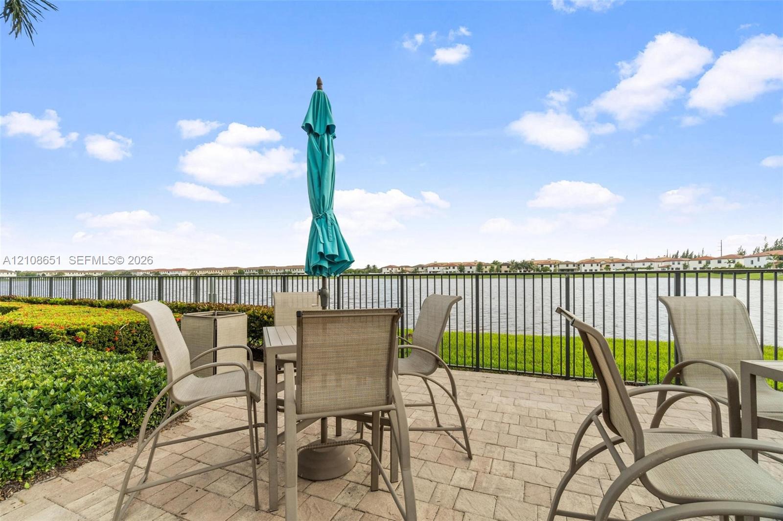 Paver patio featuring a perimeter metal fence, manicured landscaping, and direct water frontage