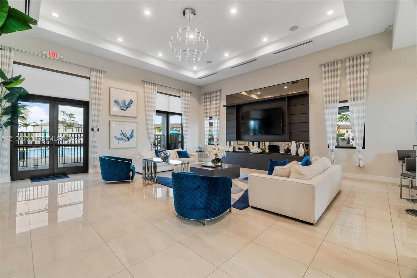 Open-concept room featuring a tiered tray ceiling, large-format tile flooring, a built-in media wall with integrated shelving, and a multi-tiered crystal chandelier