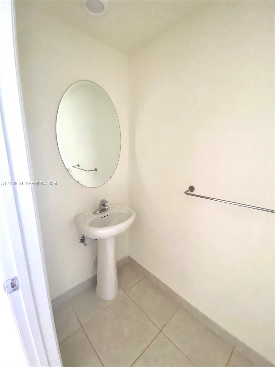 White pedestal sink with chrome faucet, oval wall-mounted mirror, and neutral-toned tile flooring