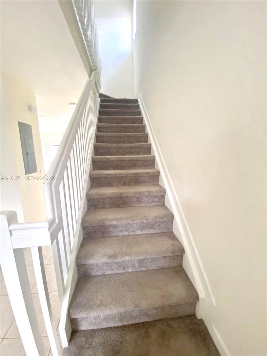 Staircase featuring neutral carpeting and white wooden handrails with vertical balusters