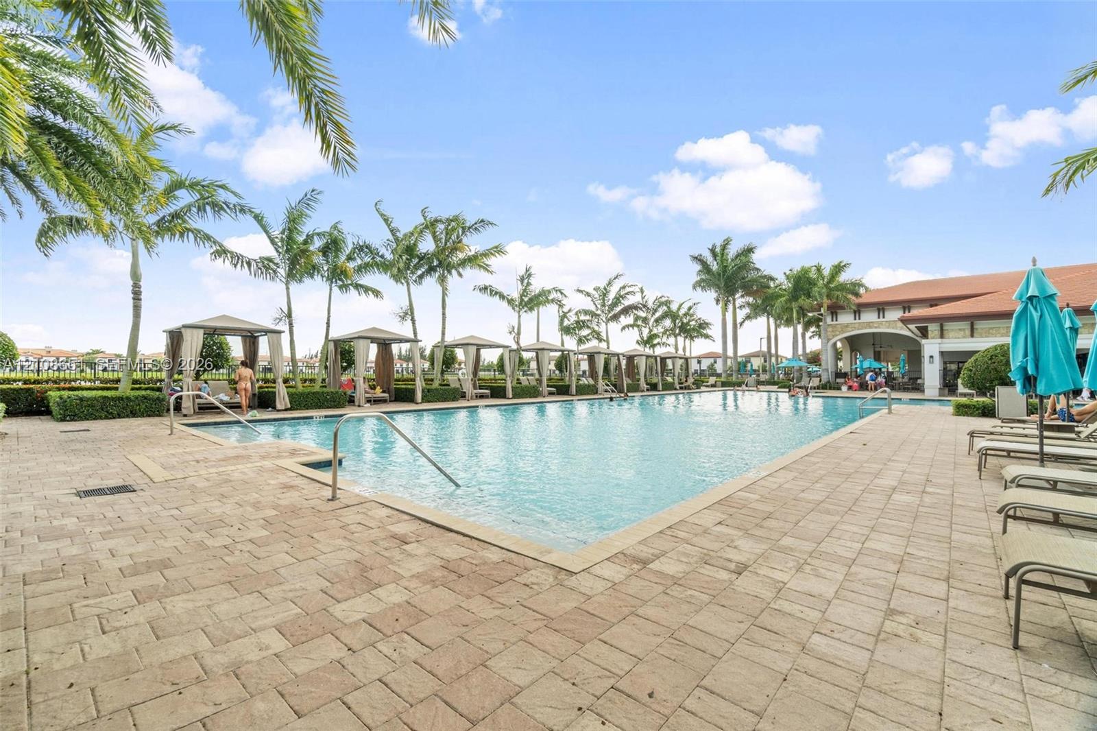 Rectangular swimming pool featuring a brick-paver deck, built-in covered cabanas, and mature palm trees