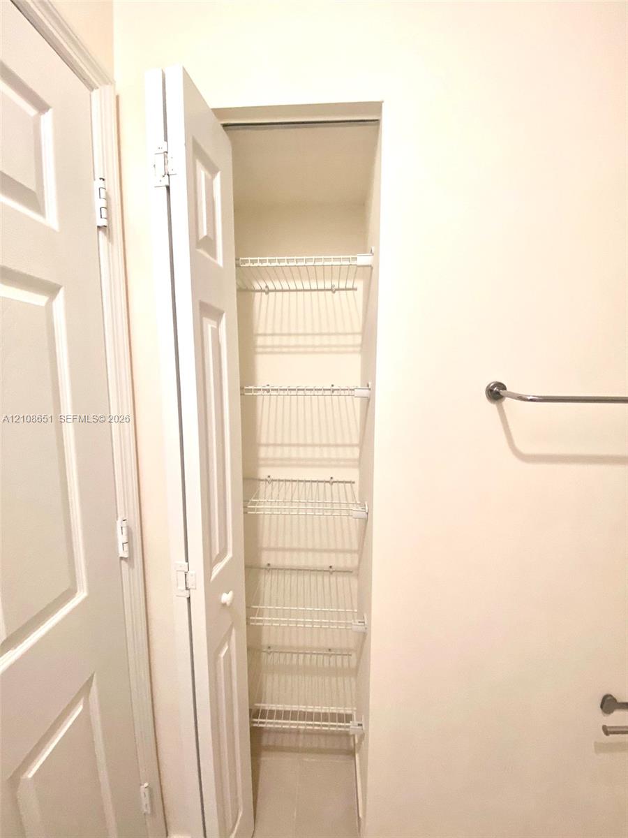 Built-in storage closet featuring five tiered wire shelves, a white paneled bifold door, and a horizontal wall-mounted towel bar