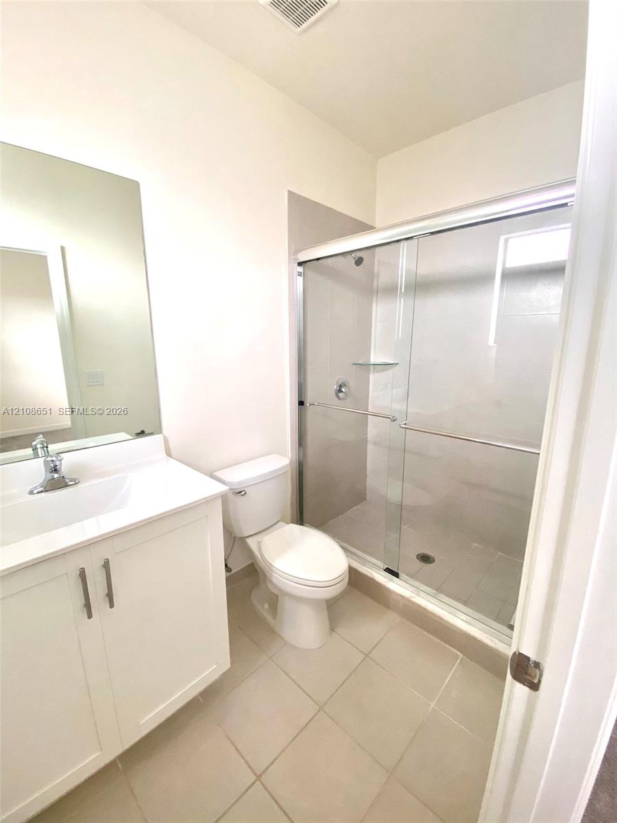 White vanity featuring a white countertop with integrated sink and chrome faucet, paired with a shower enclosure featuring sliding glass doors and neutral tile flooring