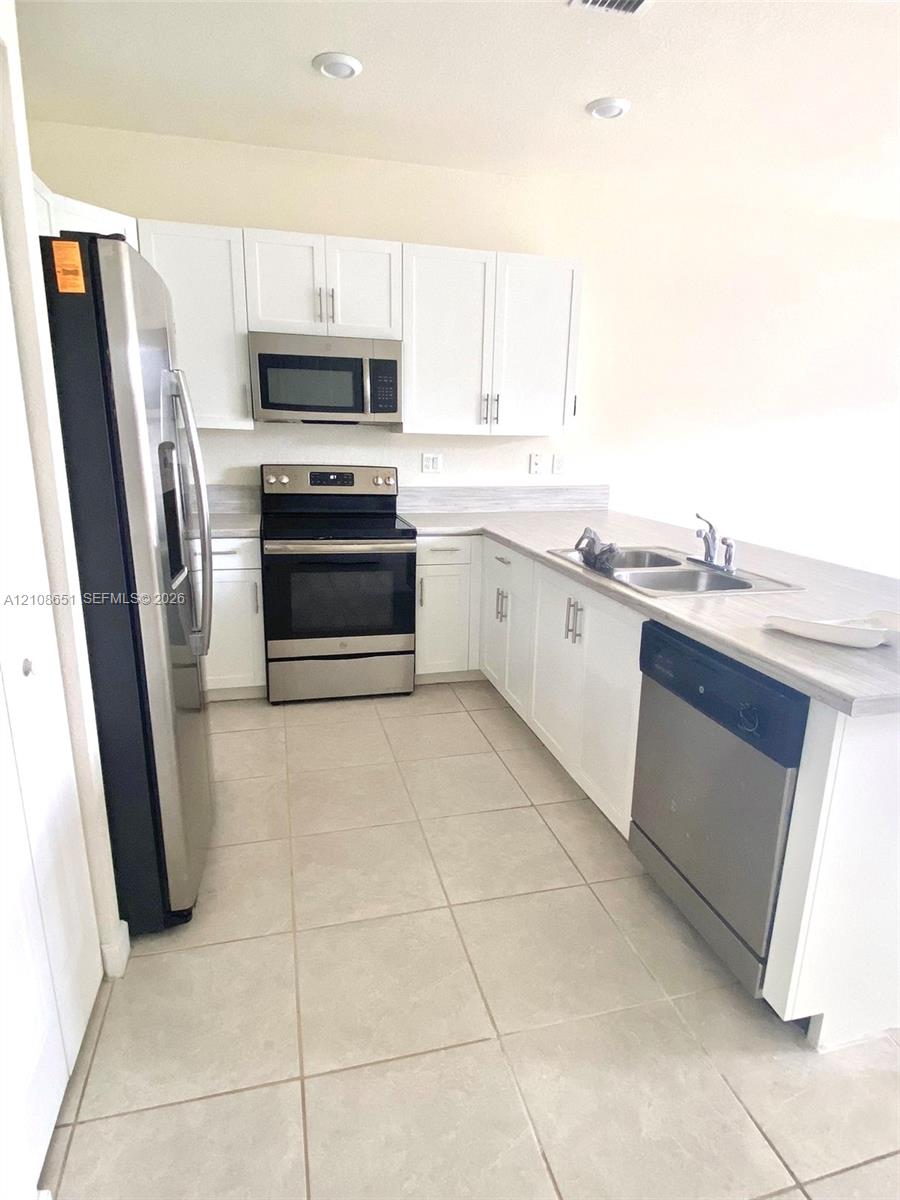 Kitchen featuring white shaker-style cabinetry, stainless steel appliances, recessed lighting, tile flooring, and a dual-basin stainless steel sink
