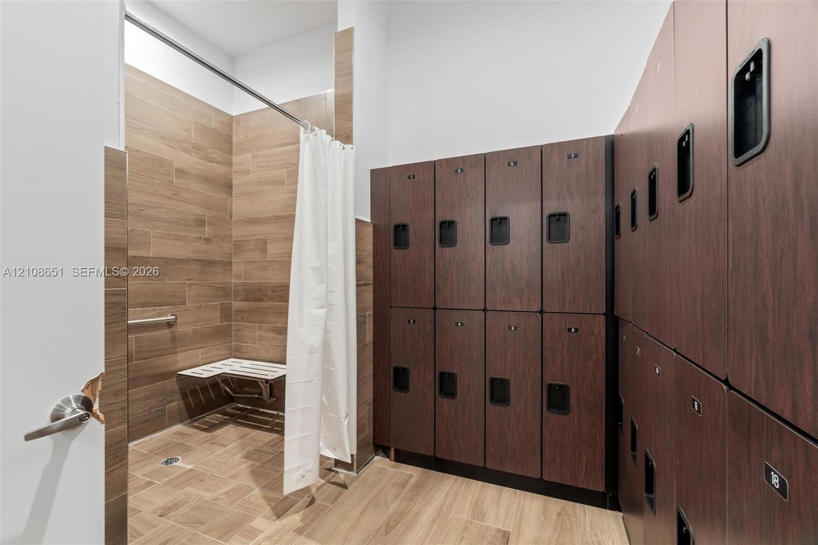 Walk-in shower featuring wood-finish tile wall and floor surfaces, wall-mounted bench, and integrated metal grab bar, accompanied by a series of built-in dark wood-finish storage lockers