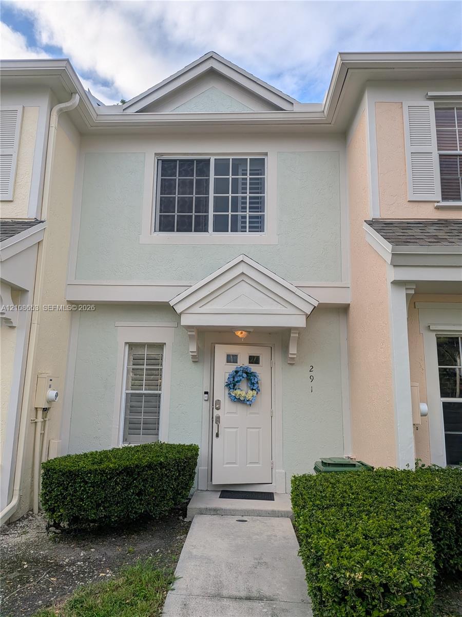 Stucco facade featuring a front-facing gable, covered entryway with decorative brackets, single-hung windows with colonial muntins, and structured landscape hedging Stucco facade featuring a front-facing gable, covered entryway with decorative brackets, single-hung windows with colonial muntins, and structured landscape hedging