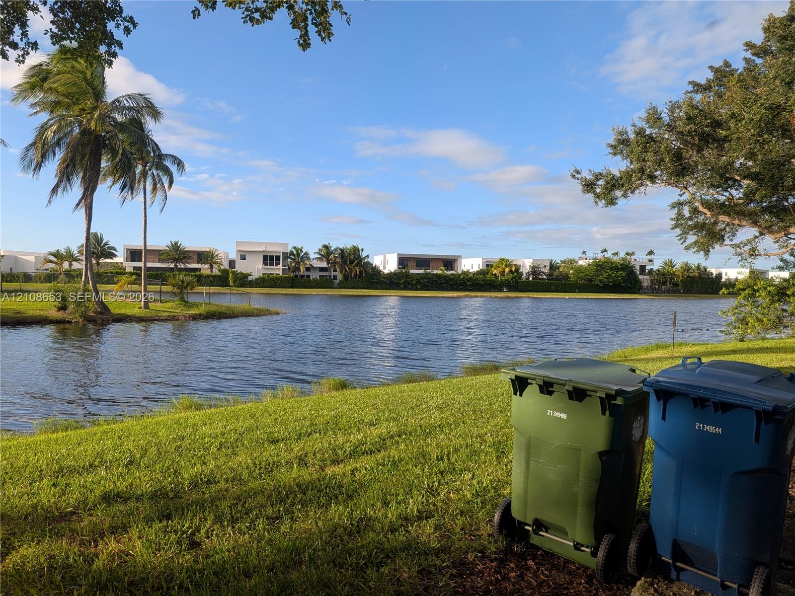 Waterfront property featuring a grassy lawn, mature palm trees, and established landscaping Waterfront property featuring a grassy lawn, mature palm trees, and established landscaping