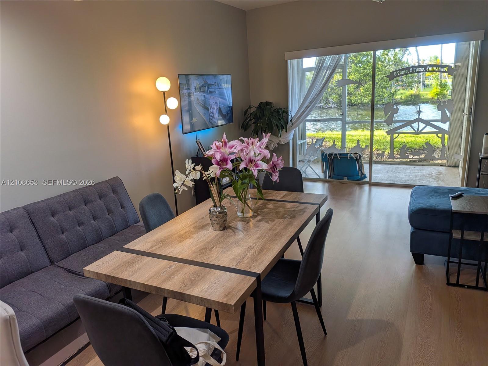 Living area featuring wood-finish flooring and large sliding glass doors leading to a screened-in patio with water frontage Living area featuring wood-finish flooring and large sliding glass doors leading to a screened-in patio with water frontage