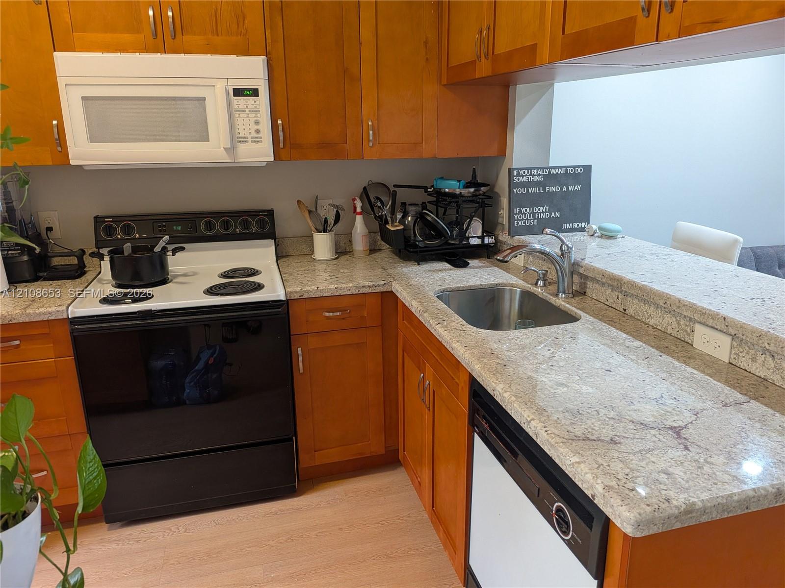 Kitchen featuring natural wood cabinetry, stone-surface countertops, an undermount stainless steel sink, a built-in microwave, and light-toned flooring Kitchen featuring natural wood cabinetry, stone-surface countertops, an undermount stainless steel sink, a built-in microwave, and light-toned flooring