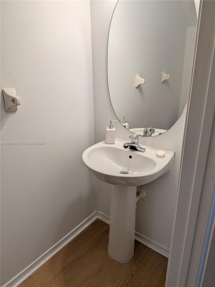 White ceramic pedestal sink featuring a polished chrome faucet, paired with an oval wall-mounted mirror and wood-finish flooring