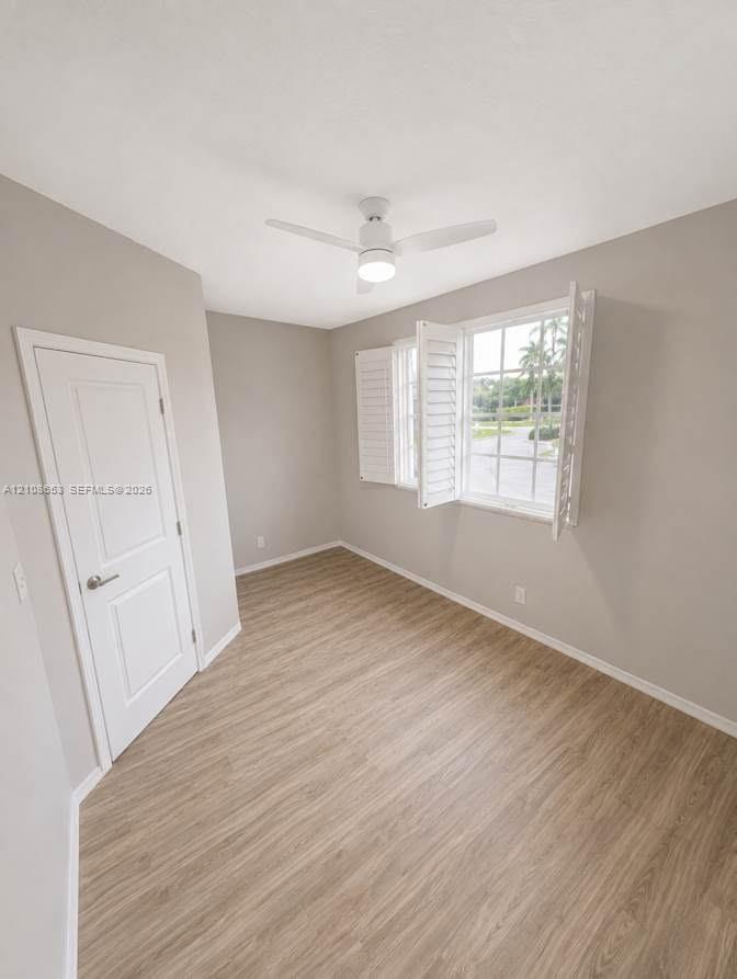 Room featuring wood-finish flooring, white plantation shutters, a white paneled door, and a ceiling fan with integrated lighting
