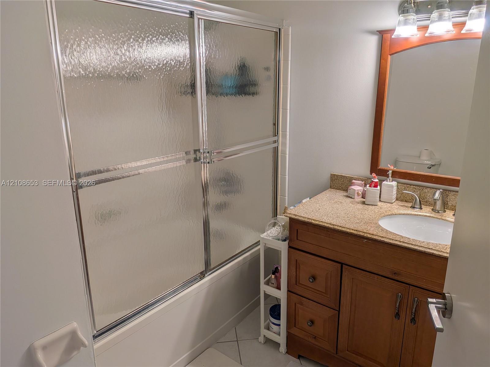 Bathroom featuring a wood vanity with a stone-finish countertop, integrated sink, metal-framed sliding glass shower door, and a wooden-framed wall mirror with integrated lighting