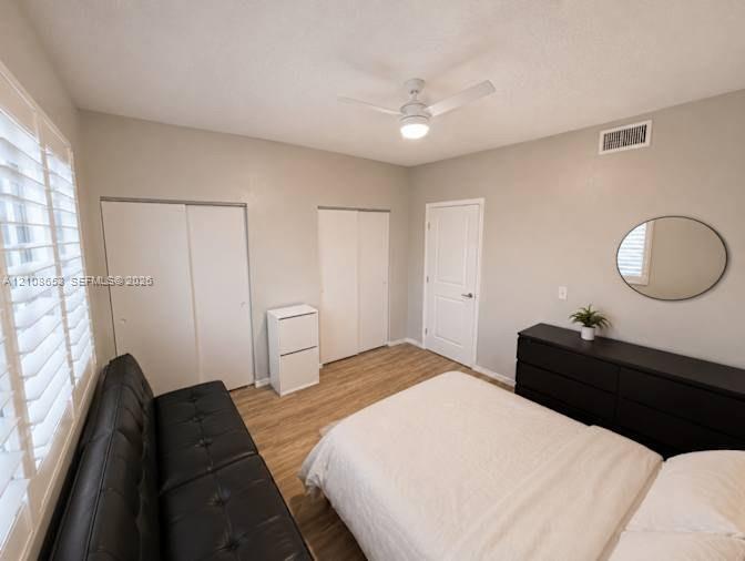 Interior space featuring wood-finish flooring, white plantation shutters, dual reach-in closets with white paneled doors, and a ceiling-mounted fan with integrated light