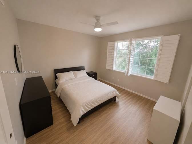 Room featuring neutral paint, wood-finish flooring, white plantation shutters, and a ceiling fan with integrated lighting
