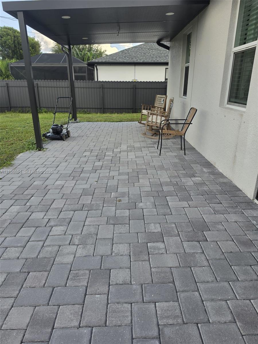 Covered rear patio featuring charcoal paver flooring, recessed lighting, and a fenced backyard