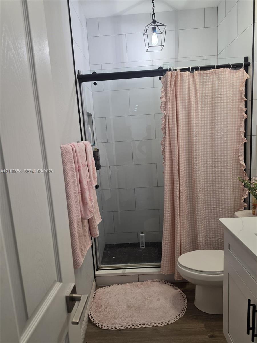 Walk-in shower with matte black sliding glass hardware and light-toned subway tile surround, complemented by a white vanity with light-toned solid surface countertop and a geometric pendant light fixture