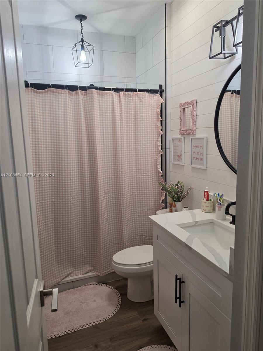 Bathroom featuring white wood-plank wall detailing, a vanity with a stone countertop, an integrated rectangular sink, matte black hardware, and geometric pendant lighting