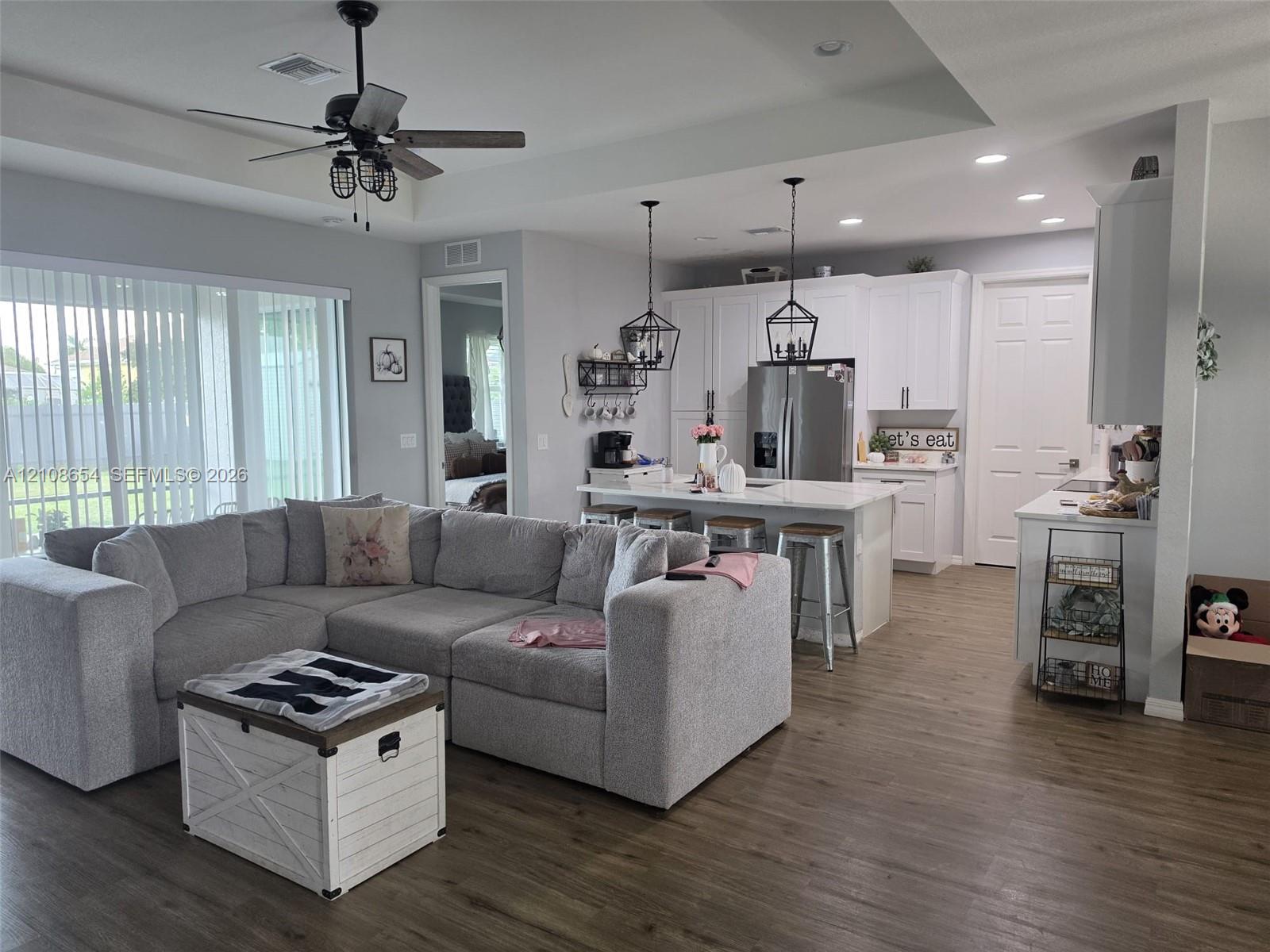 Open-concept kitchen featuring white shaker-style cabinetry, quartz countertops, a central island, and wood-finish flooring throughout