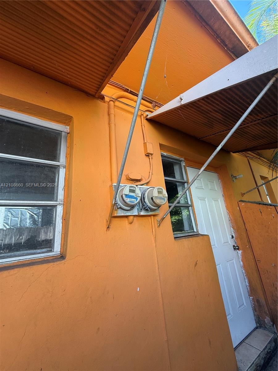 Exterior view featuring a stucco finish, dual-panel utility meters, a paneled entry door, and metal awning structures