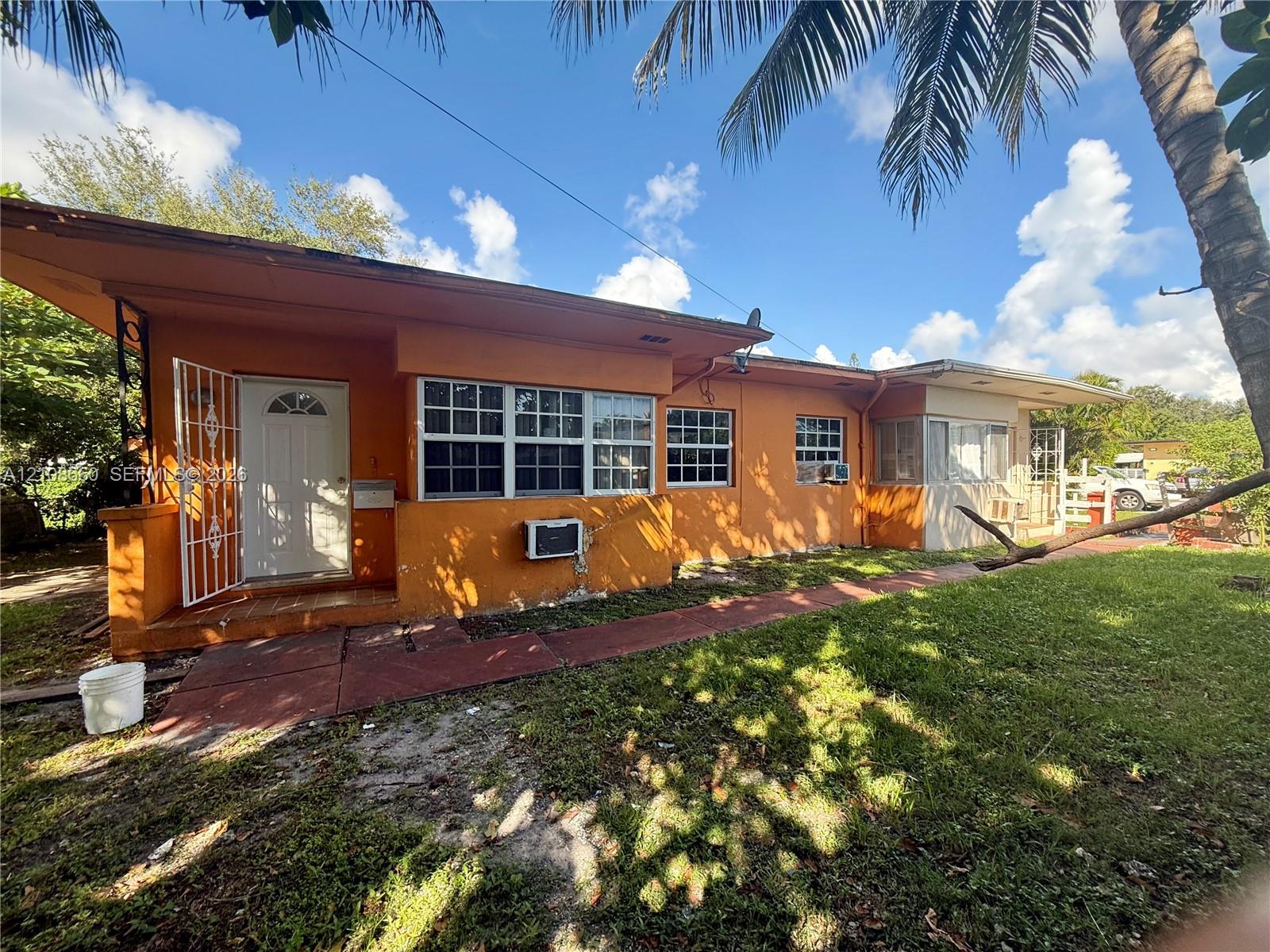 Single-story exterior featuring a stucco facade, metal security screen door, multi-pane windows, and a paved walkway