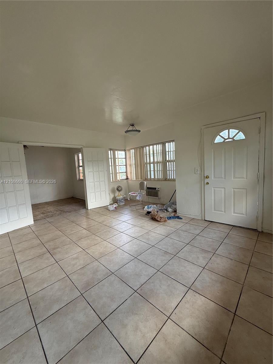 Interior space featuring neutral tile flooring, multiple sets of glass-paneled double doors, horizontal window blinds, and an exterior door with an arched glass insert