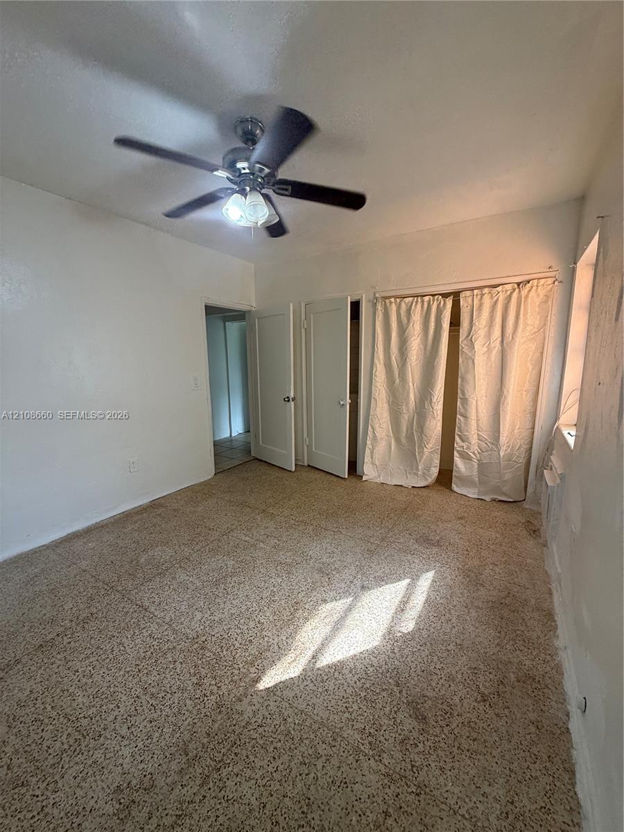 Interior space featuring speckled tile flooring, two solid-core doors, and a ceiling-mounted light fixture with a multi-blade fan
