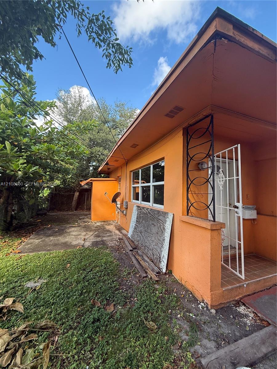 exterior featuring an attached covered entryway with decorative metal screening, tile porch flooring, and an exterior storage structure