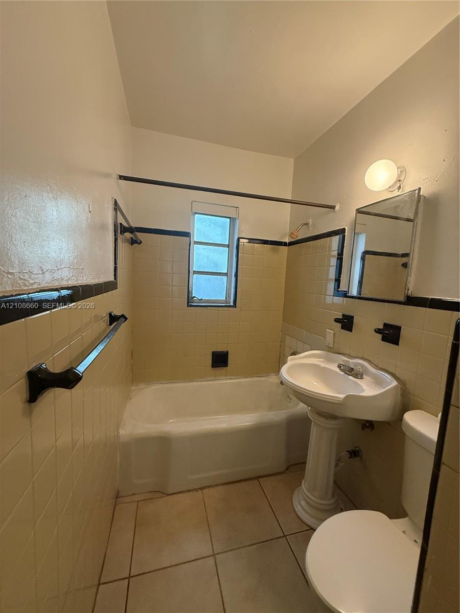 Bathroom featuring a pedestal sink, a deep-basin tub with tile surround, black tile accents, and tiled flooring