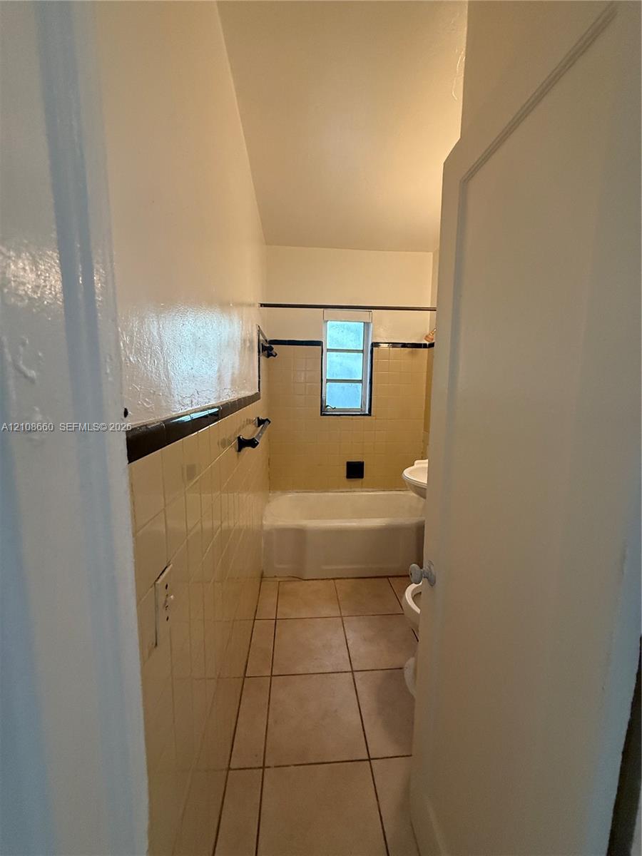 Full bathroom featuring tile flooring, a porcelain bathtub, wall-mounted hardware, and decorative tile accent detailing