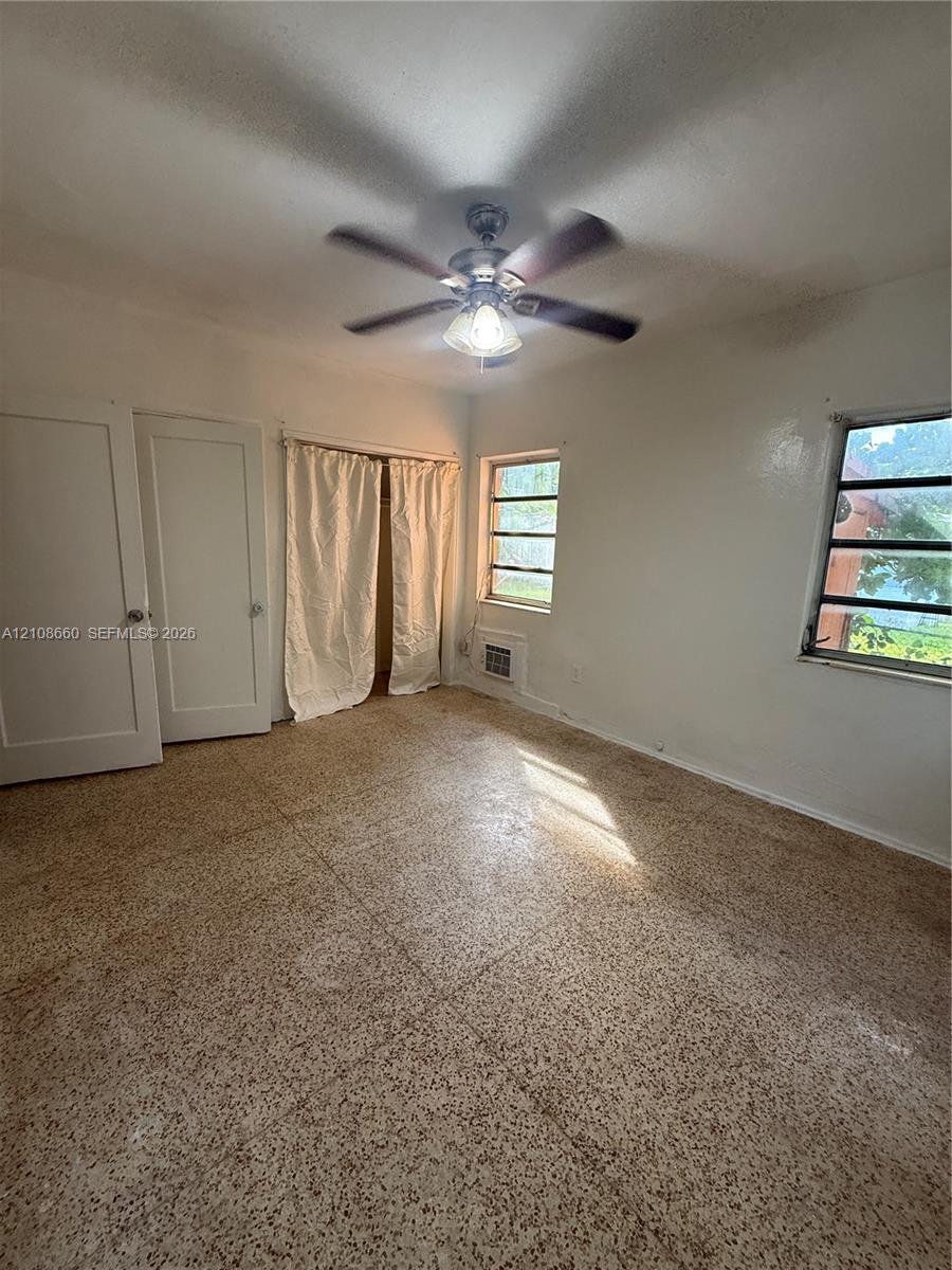 Interior space featuring terrazzo flooring, dual-panel doors, horizontal sliding windows, and a ceiling-mounted light fixture with a multi-blade fan