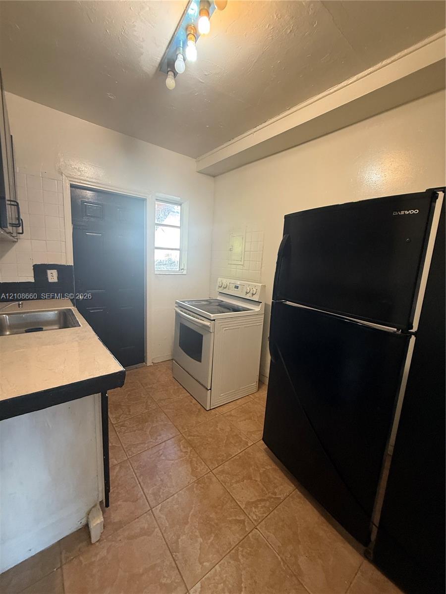 Kitchen featuring ceramic tile flooring, a white electric range, a stainless steel sink, and light-toned countertops with dark edging
