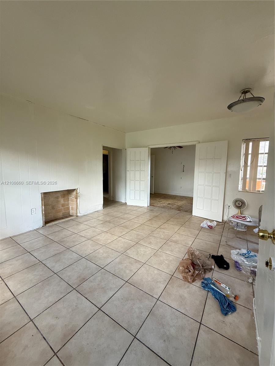 Neutral-toned tile flooring, masonry fireplace hearth, and double French doors with glass panes
