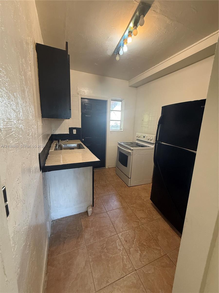 Kitchen featuring ceramic tile flooring, built-in cabinetry, tiled backsplash, and stainless steel sink
