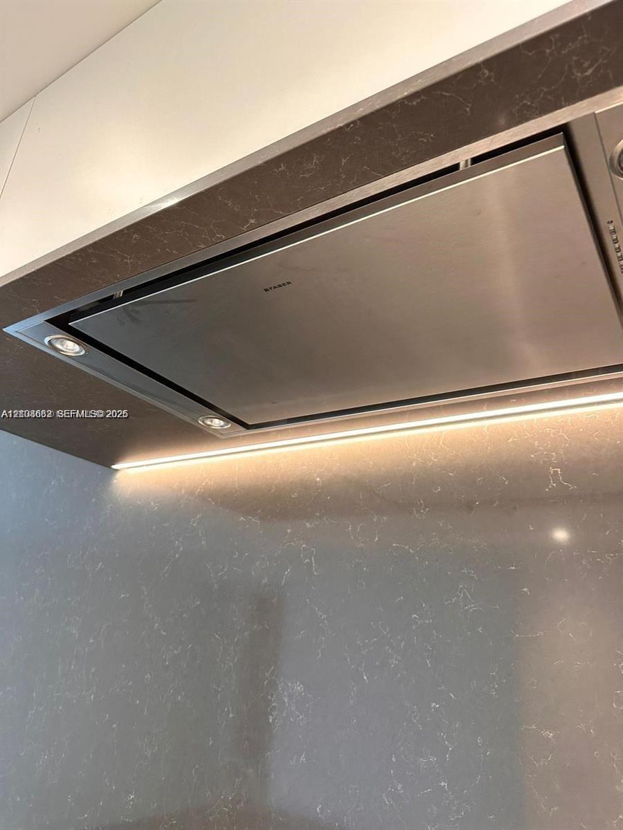 Stainless steel range hood integrated into a custom enclosure featuring solid-surface surfacing, recessed task lighting, and under-cabinet strip lighting