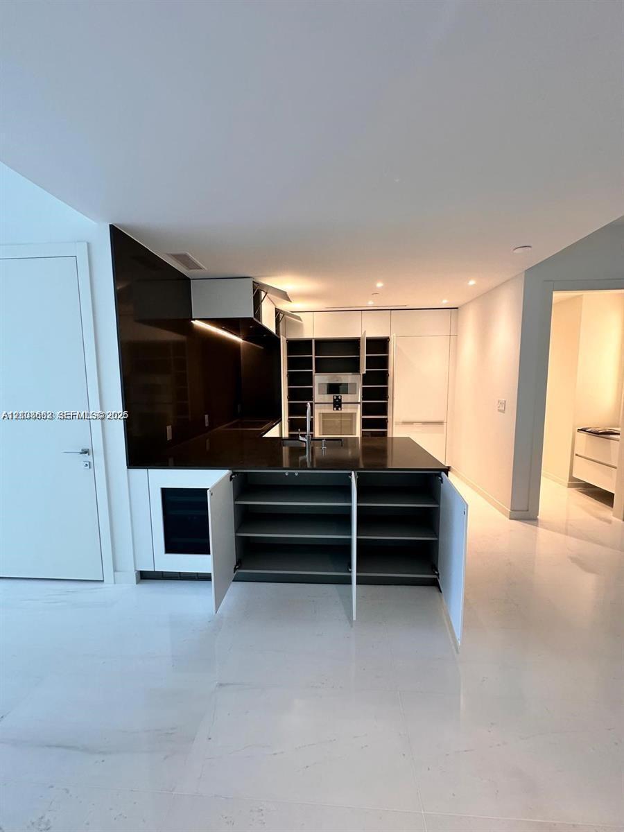 Kitchen featuring high-contrast cabinetry, integrated appliances, dark stone-finish countertops, an under-counter wine cooler, and polished light-toned flooring