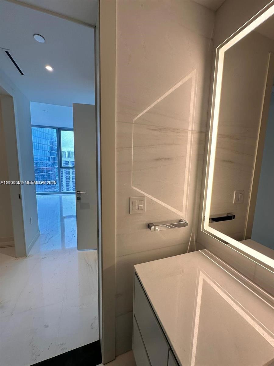 Bathroom vanity featuring a stone-composite countertop, full-height stone wall cladding, and an integrated backlit mirror
