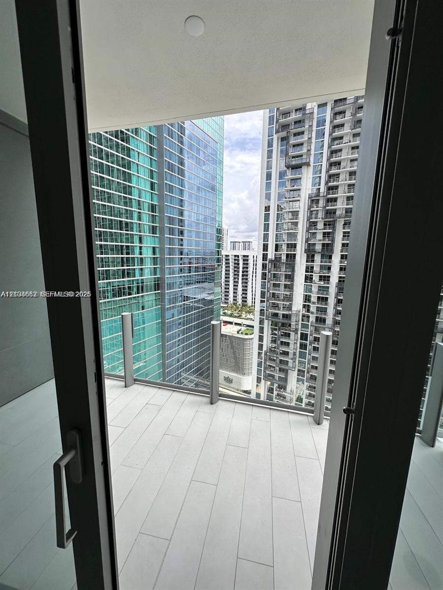 Private balcony featuring light-toned, large-format tile flooring and a minimalist glass-panel railing with metal supports
