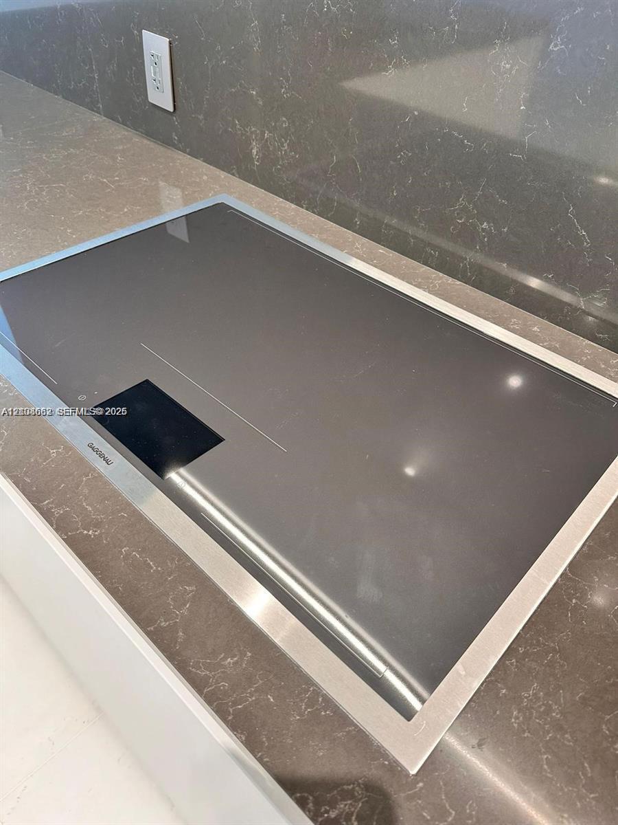 Flush-mount induction cooktop featuring a sleek glass surface with a stainless steel trim, integrated into a neutral-toned countertop with a matching slab backsplash