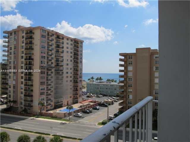 Exterior balcony featuring a metal railing and an outlook toward the ocean, neighboring high-rise structures, and street-level hardscaping Exterior balcony featuring a metal railing and an outlook toward the ocean, neighboring high-rise structures, and street-level hardscaping