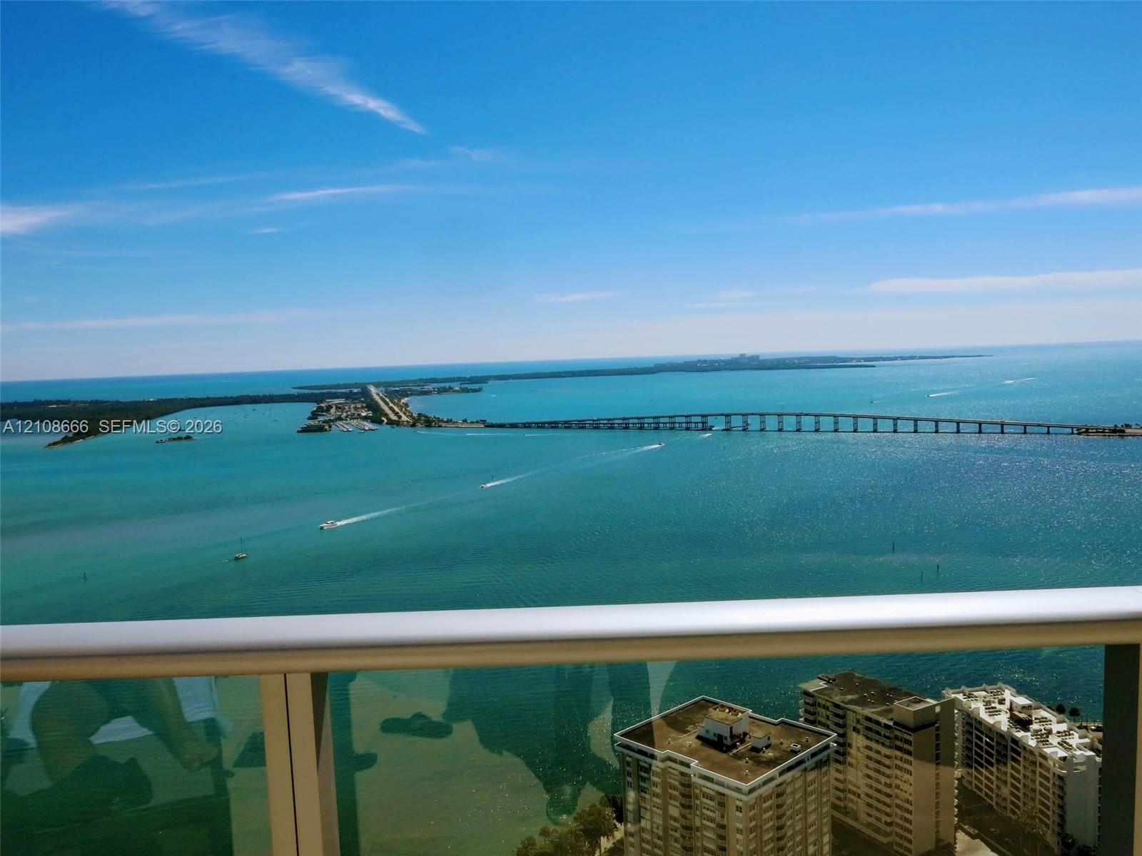 High-rise balcony featuring a metal railing with glass panels, showcasing panoramic coastal scenery, open water, and a bridge