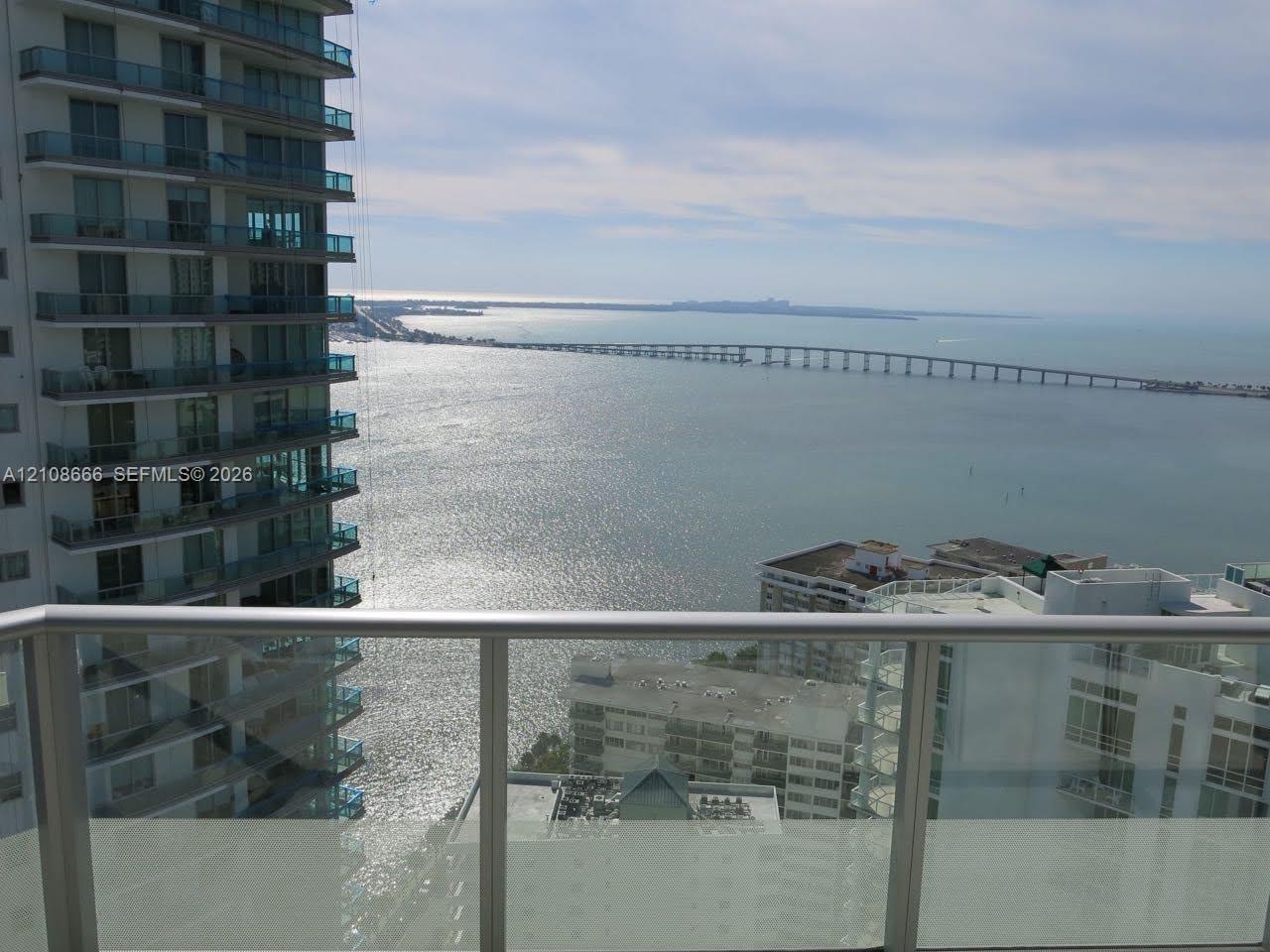 Balcony featuring glass railings, metal framing, and direct water and bridge scenery Balcony featuring glass railings, metal framing, and direct water and bridge scenery