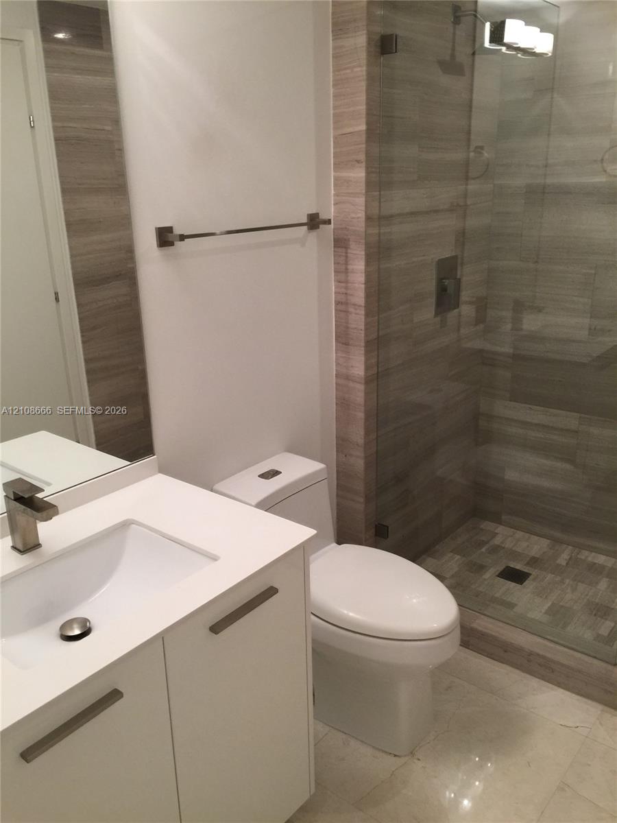 Modern bathroom featuring a white vanity with a rectangular basin, metallic single-handle faucet, glass-enclosed shower with tiled surround, and integrated lighting